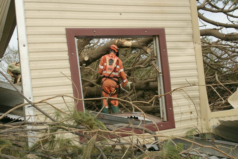 An emergency worker cutting fallen trees. The worker is framed through a window.